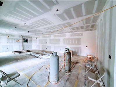 Fresh drywall installation with finished seams and smooth ceiling in a large open room.