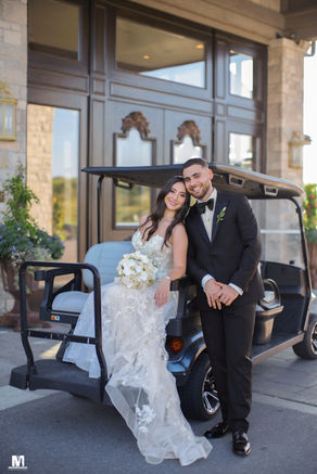 Couple posing indoors beside large windows and floral arrangements.