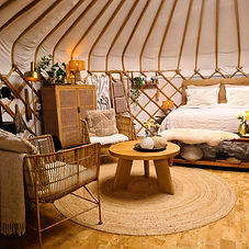 Yurt Sirius van binnen vanaf de deur - zithoek en bed in een serene ronde ruimte met natuurlijke lichtinval.