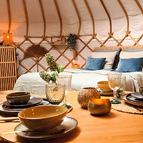 Gedekte tafel in Yurt Orion met kleurrijk servies en het opgemaakte bed op de achtergrond.