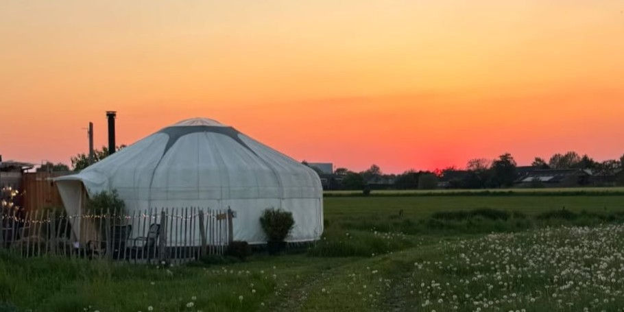 Yurt Venus bij zonsondergang onder een warme oranje lucht in het Achterhoekse landschap.