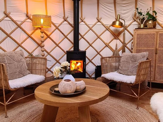 Zithoek van Yurt Sirius met brandende houtkachel, warme plaids en rustige tinten.