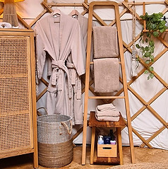Beige badjassen en handdoeken liggen klaar in Yurt Sirius, passend bij het lichte en serene interieur.