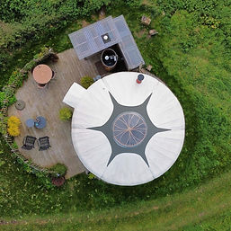 Yurt Orion met terras ligt omgeven door groen in het landschap - de ronde vormen zijn van bovenaf goed te zien.