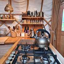 De keuken van Yurt Orion met gasfornuis en plankjes gevuld met zorgvuldig gekozen essentials.