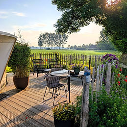 Terras van yurt Orion in ochtendzon, ingericht met eettafel en loungeset voor buitenleven in alle rust.