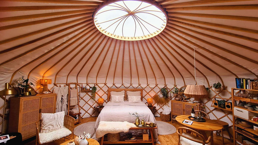 Breedbeeld van het volledige interieur van Yurt Sirius met bed, zithoek, eettafel en ronde open leefruimte.