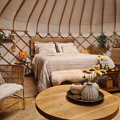 Het bed van Yurt Sirius is opgemaakt met licht linnen beddengoed in zachte beige en witte tinten.