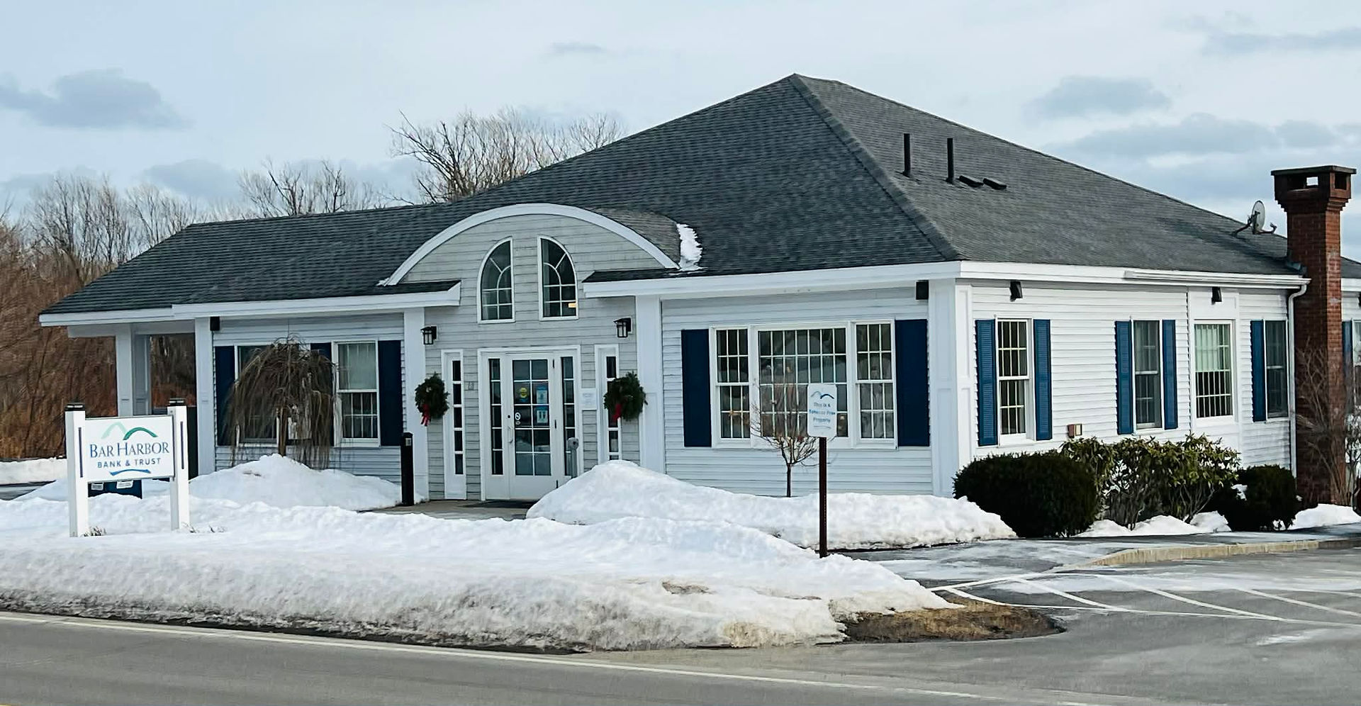 Bar Harbor Bank & Trust branch in Lubec, Maine, a white building with blue shutters and snowbanks along the road.
