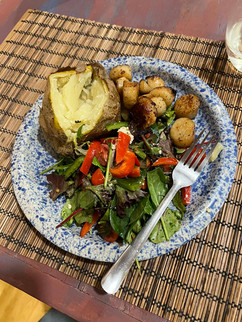 Blue speckled plate with a baked potato, seared scallops, and mixed green salad with cherry tomatoes and red peppers, fork resting on the plate.