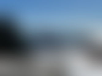 A red-and-white striped lighthouse beside a white house overlooking the ocean, with snow on the ground and sunlight reflecting off the water.