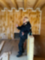 Bill Clark stands with a champagne glass inside the unfinished interior of Clark’s Folly, wood beams exposed.