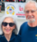 Bill and Patricia smiling together in front of the West Quoddy Station sponsor banner at the Bay of Fundy International Marathon finish line in Lubec.