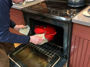 Man placing a red Le Creuset pot into an oven in a home kitchen.