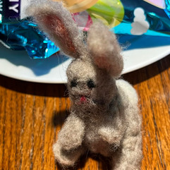 Small handmade felt bunny sitting on a wooden table beside Easter candy