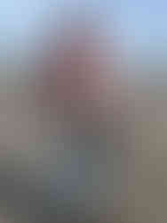 A man smiling on the beach with a clam basket in hand and ocean behind him.