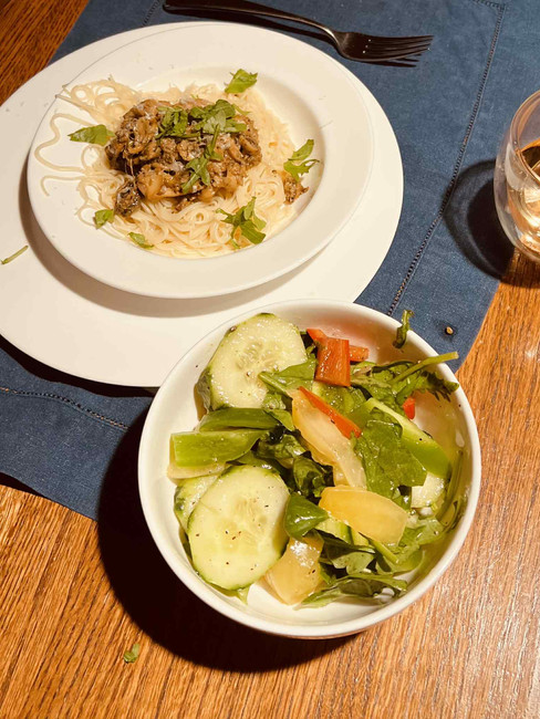 A plate of pasta topped with steamer clams and a bowl of salad on a wooden table.
