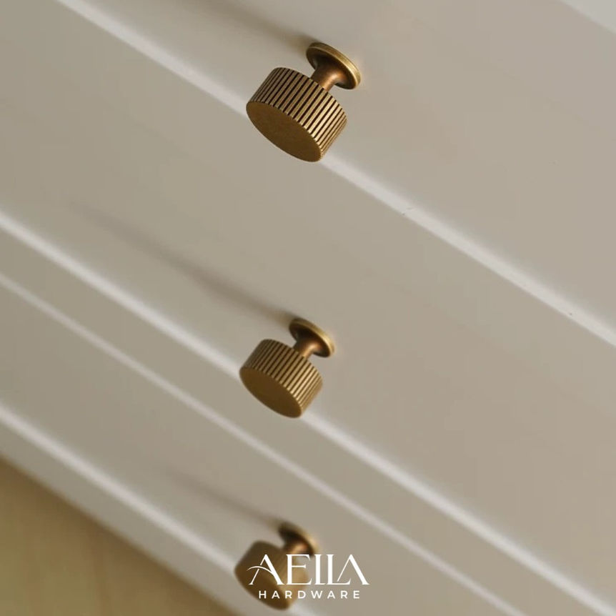 ลูกบิดสีทองสามอันติดอยู่บนบานตู้สีขาว AELLA HARDWARE