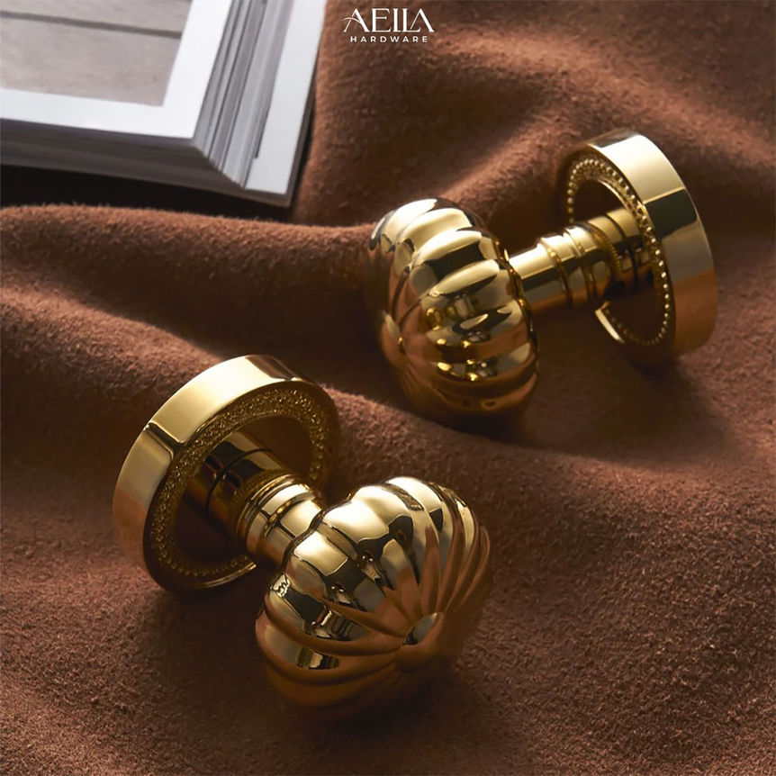 มือจับเฟอร์นิเจอร์แบบกลมสองอันสีทองเงางาม AELLA HARDWARE บนผ้าสีน้ำตาล