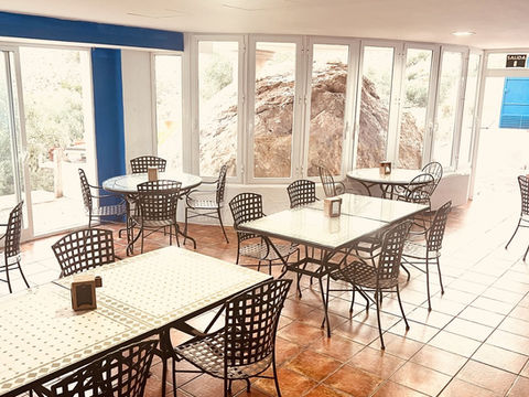 Comedor interior con mesas, sillas y grandes ventanales.