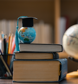 A small Earth-globe toy with a small graduation cap on its top. The glob is standing over three books