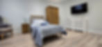 An image of a bedroom with a large bed with luxurious bedding, a bedside table with elegant lamp on, a double wardrobe, tasteful decorations, on large TV on the wall and a comfortable arm chair at Shedfield Lodge Dementia Specialist Care Home near Wickham 