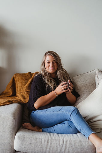 Greta-dawson-from-beyond-loved-sitting-on-the-couch-with-a-mug-in-her-hand-smiling-at-the-camera-somatic-healing-clearing-energy-blocks