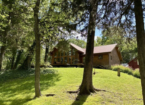 Wooded hillside with a cedar sided main house surrounded by trees and green lawn