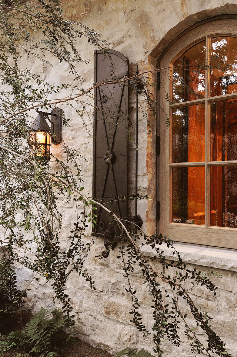 Stone wall with arched window and black iron shutter. Architectural photograph by Gina Taro