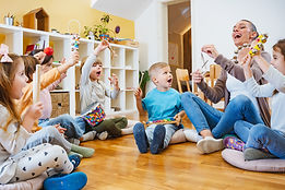 Kindergarten teacher with children sitting on the floor having music class, using various