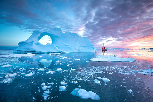 Little red sailboat cruising among floating icebergs in Disko Bay glacier during midnight