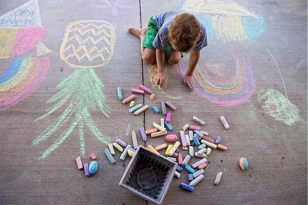 Young child drawing on sidewalk with chalk in the warm weather