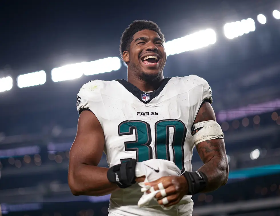 Football player in white and green uniform smiling under stadium lights.