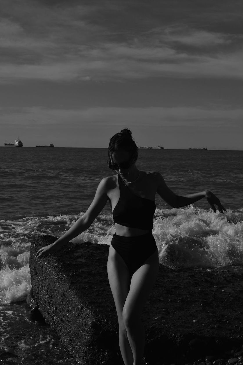 woman standing on beach, waves in background, black and white
