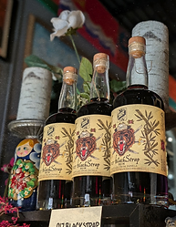 3 bottles of 3BR Distillery's 017 BLACKSTRAP rum. The bottles have a pale yellow label with a pirate bear head with an eye patch, three swords, and bamboo on the sides. The bottles are on a shelf next to a matryoshka doll.