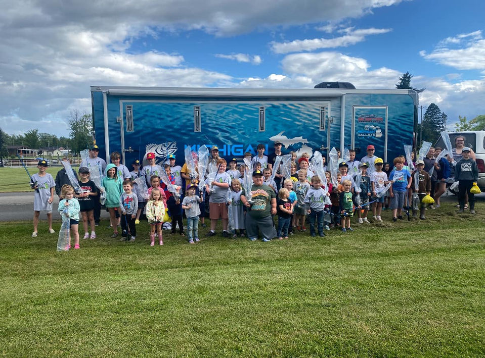 group of children holding fishing rods in front of event trailer
