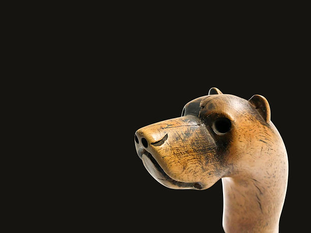Left-facing close-up of the carved hound's head and face on an Eastern Woodlands effigy crooked knife, circa 1850-1880, featuring wood, brass wire, and hide.
