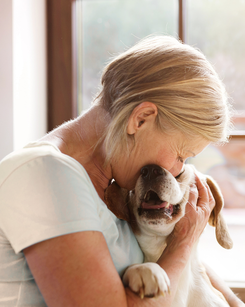 A woman holding her dog close, face pressed gently against the dog's head. A moment of quiet love and comfort after a canine cancer diagnosis.