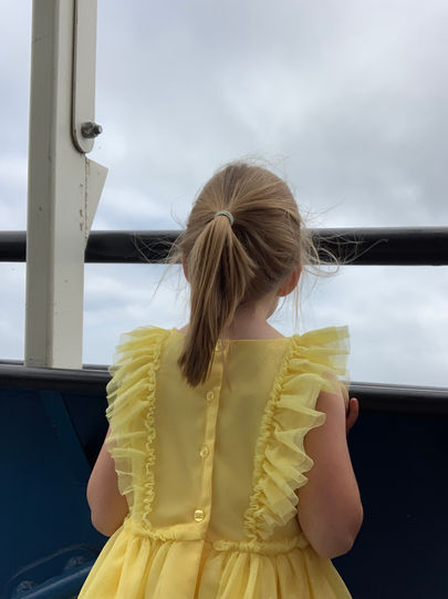 Little blonde girl in yellow dress overlooking the water on a boat