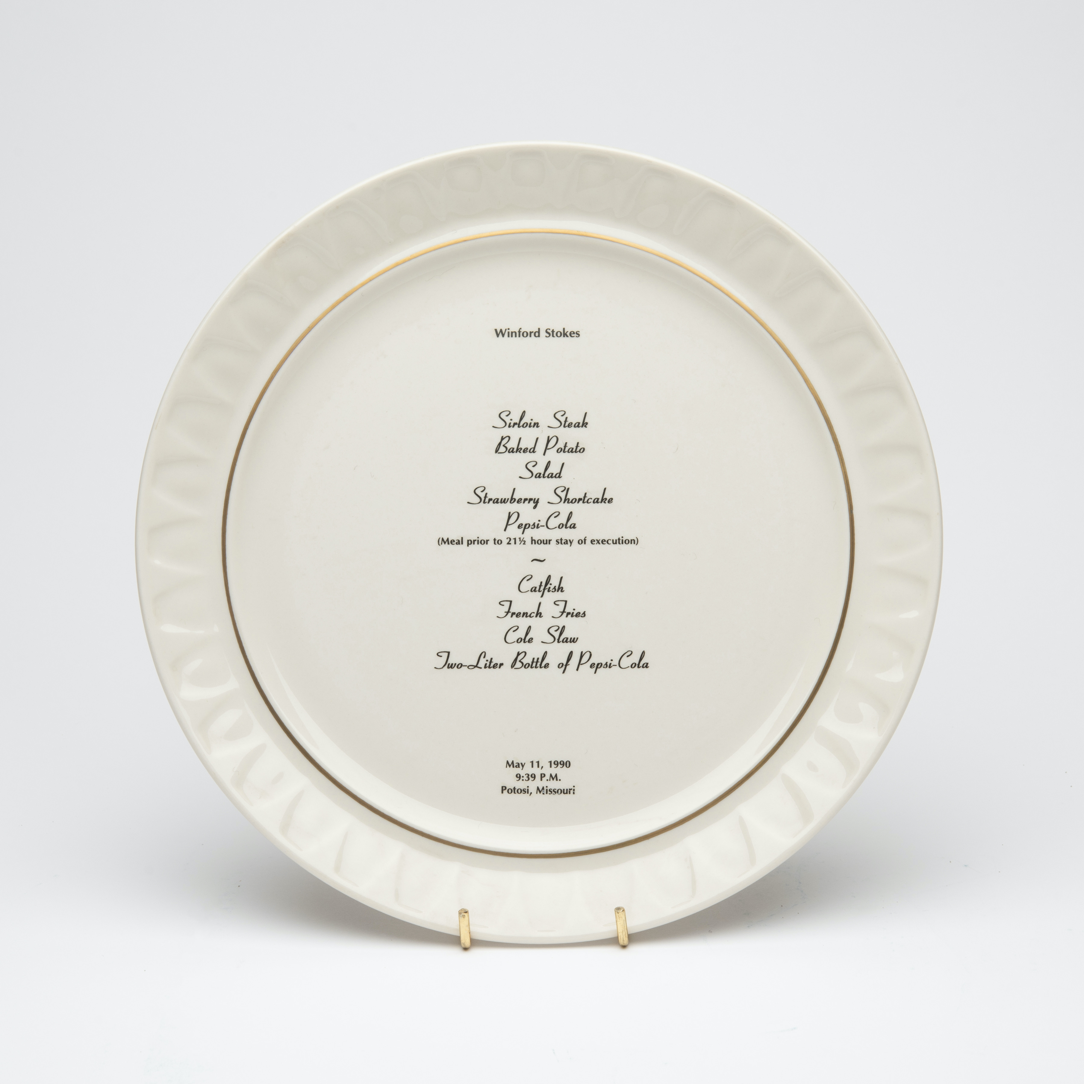 Bone china dinner plate, with gold trim and text printed in center. Text includes a description of the last meal requested and served to someone prior to their execution. The name of the person, time, date and place of execution is also printed on the plate.