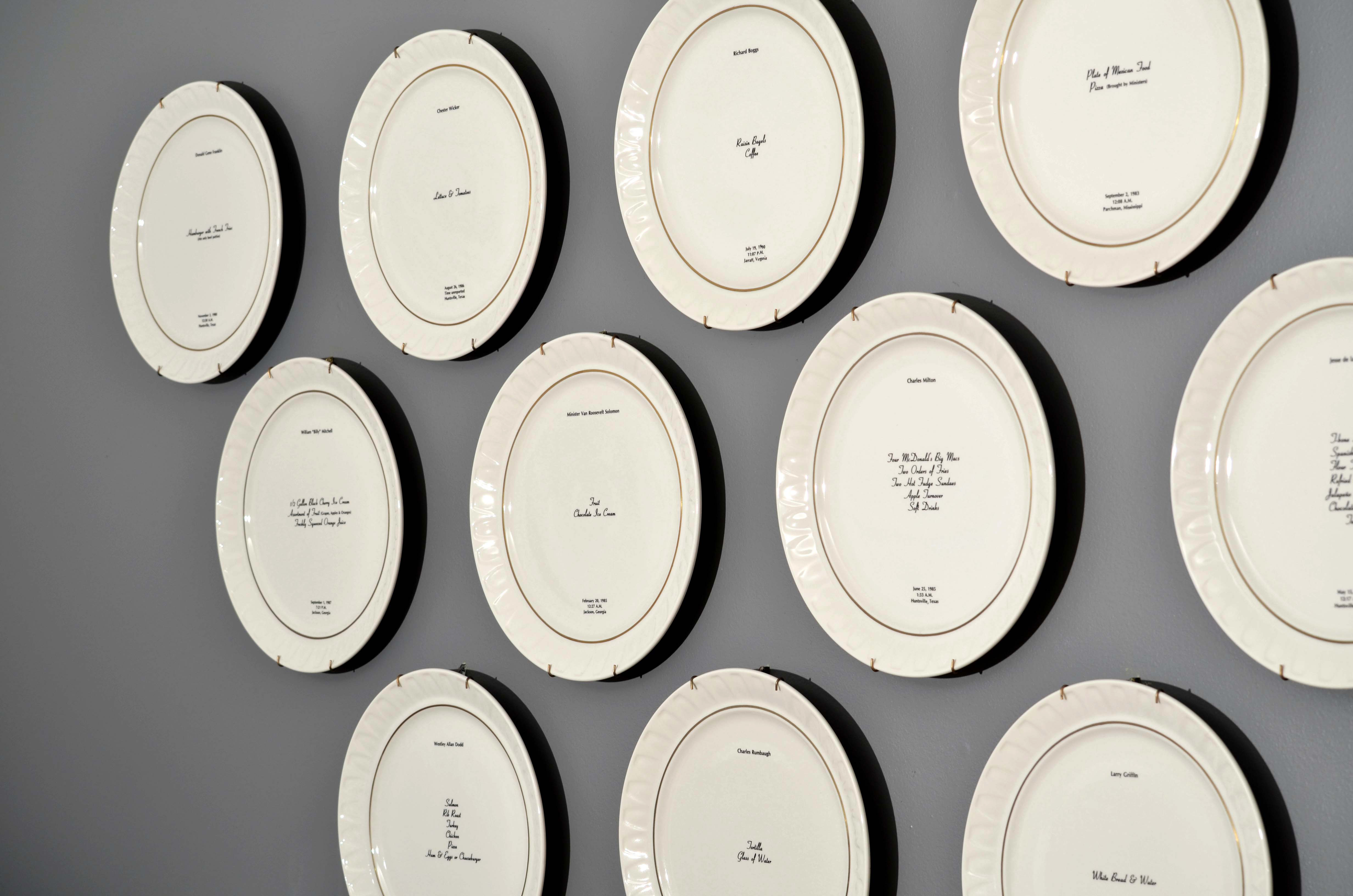 Bone china dinner plate, with gold trim and text printed in center. Text includes a description of the last meal requested and served to someone prior to their execution. The name of the person, time, date and place of execution is also printed on the plate. Detail from wall installation.