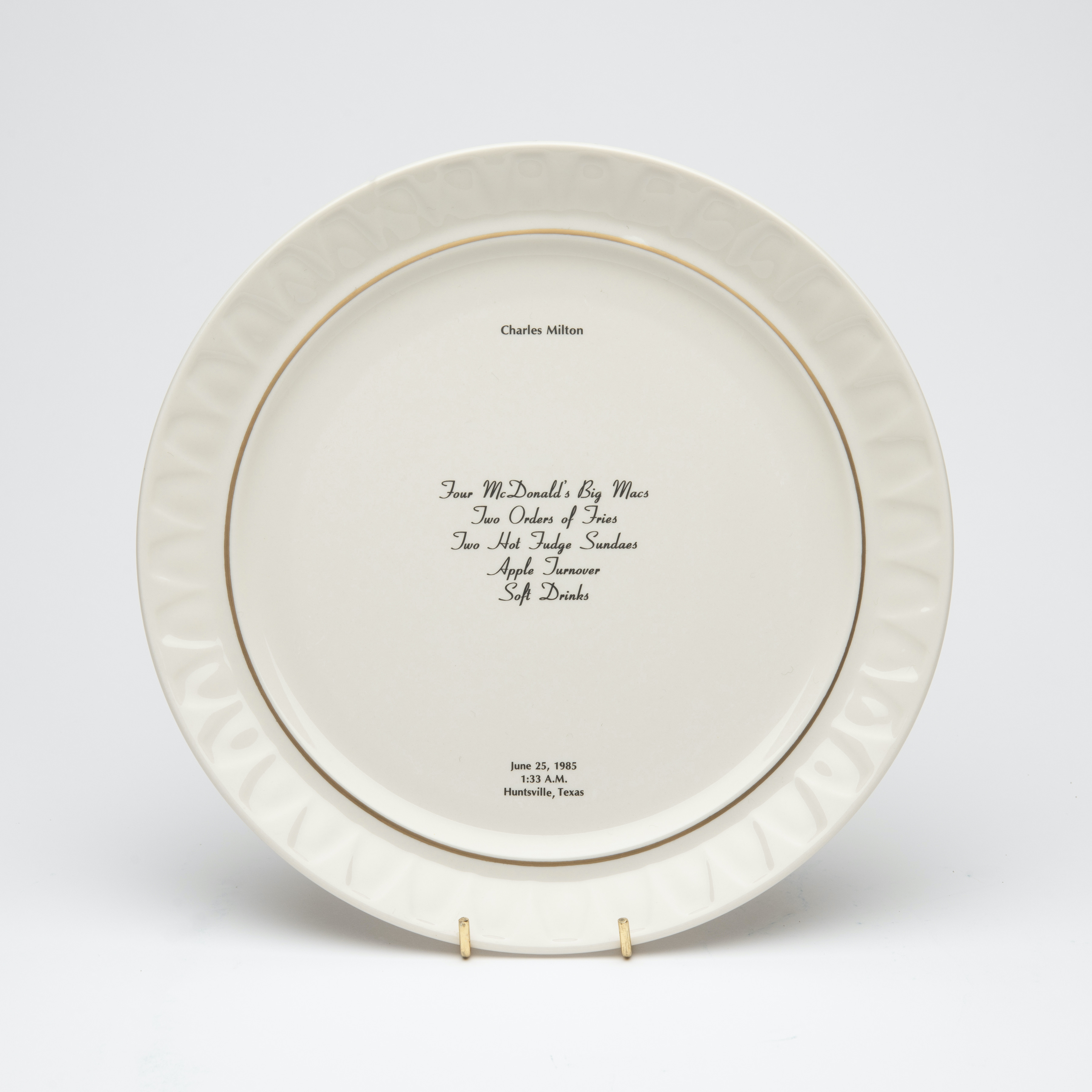 Bone china dinner plate, with gold trim and text printed in center. Text includes a description of the last meal requested and served to someone prior to their execution. The name of the person, time, date and place of execution is also printed on the plate.