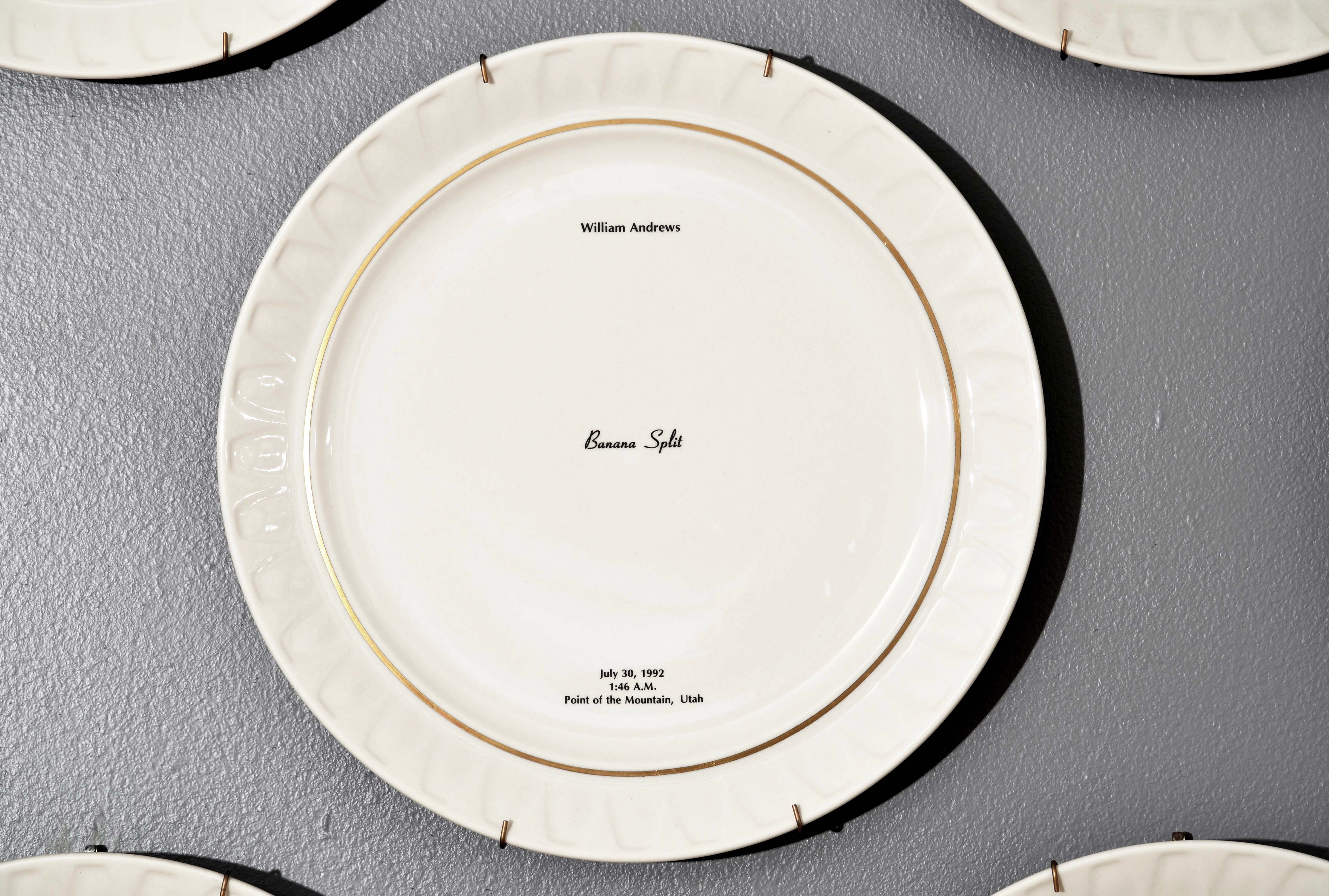 Bone china dinner plate, with gold trim and text printed in center. Text includes a description of the last meal requested and served to someone prior to their execution. The name of the person, time, date and place of execution is also printed on the plate. Detail from installation.