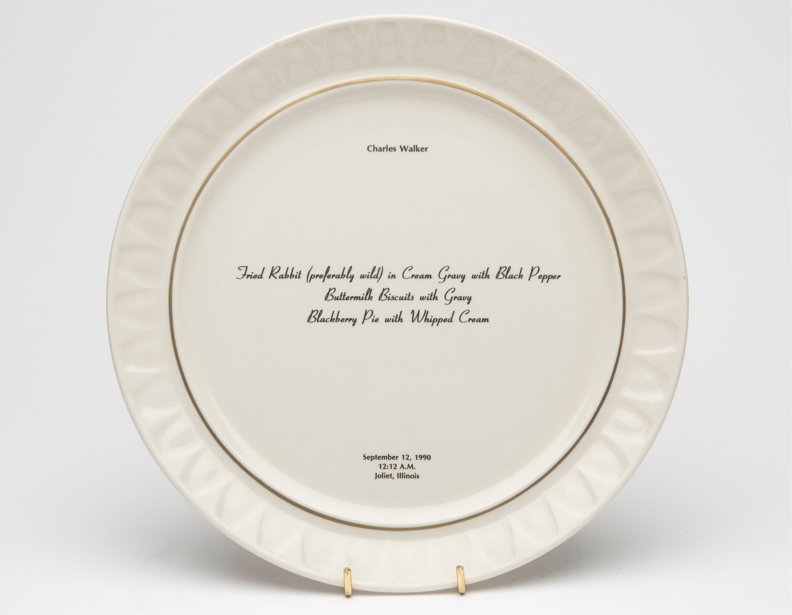 Bone china dinner plate, with gold trim and text printed in center. Text includes a description of the last meal requested and served to someone prior to their execution. The name of the person, time, date and place of execution is also printed on the plate.