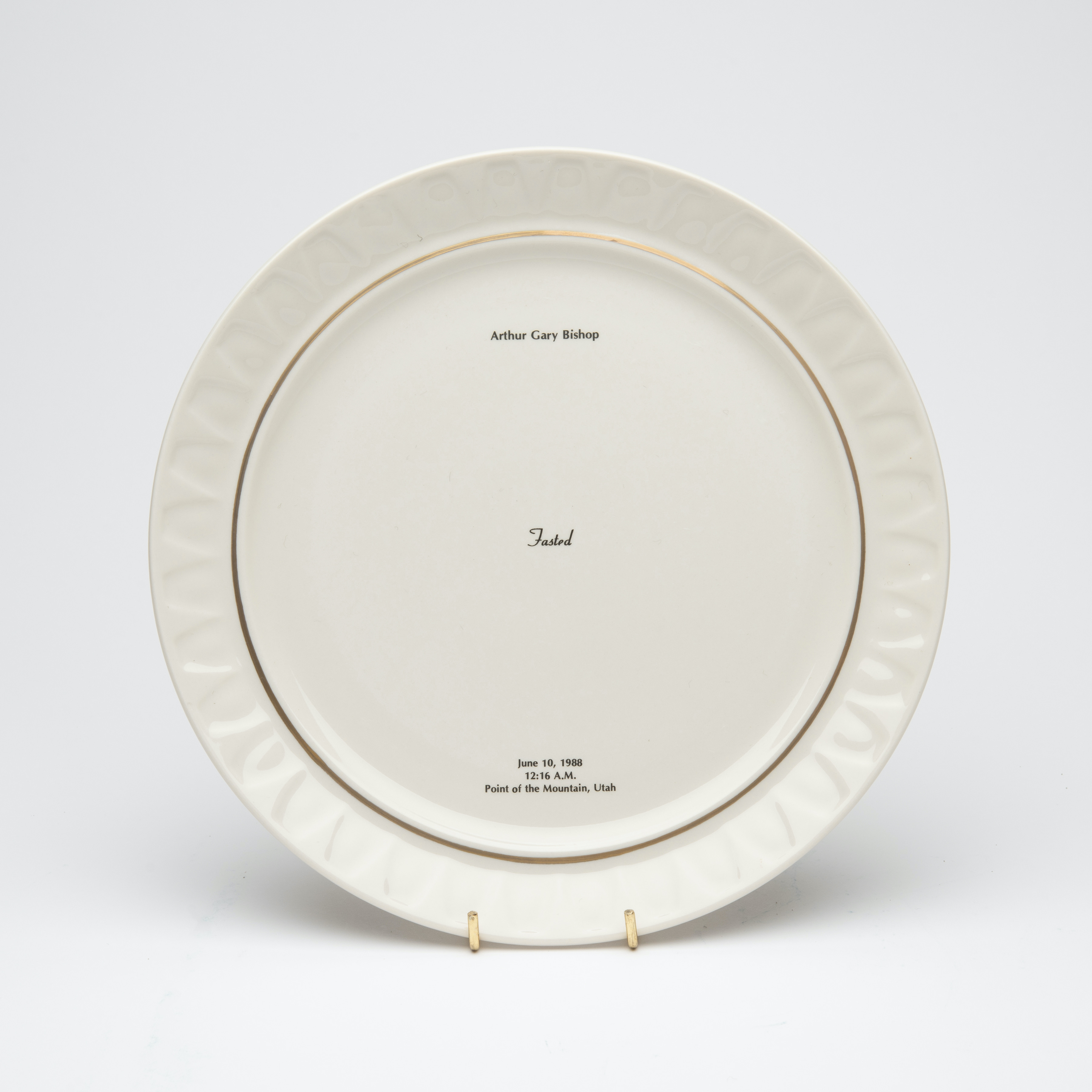Bone china dinner plate, with gold trim and text printed in center. Text includes a description of the last meal requested and served to someone prior to their execution. The name of the person, time, date and place of execution is also printed on the plate.