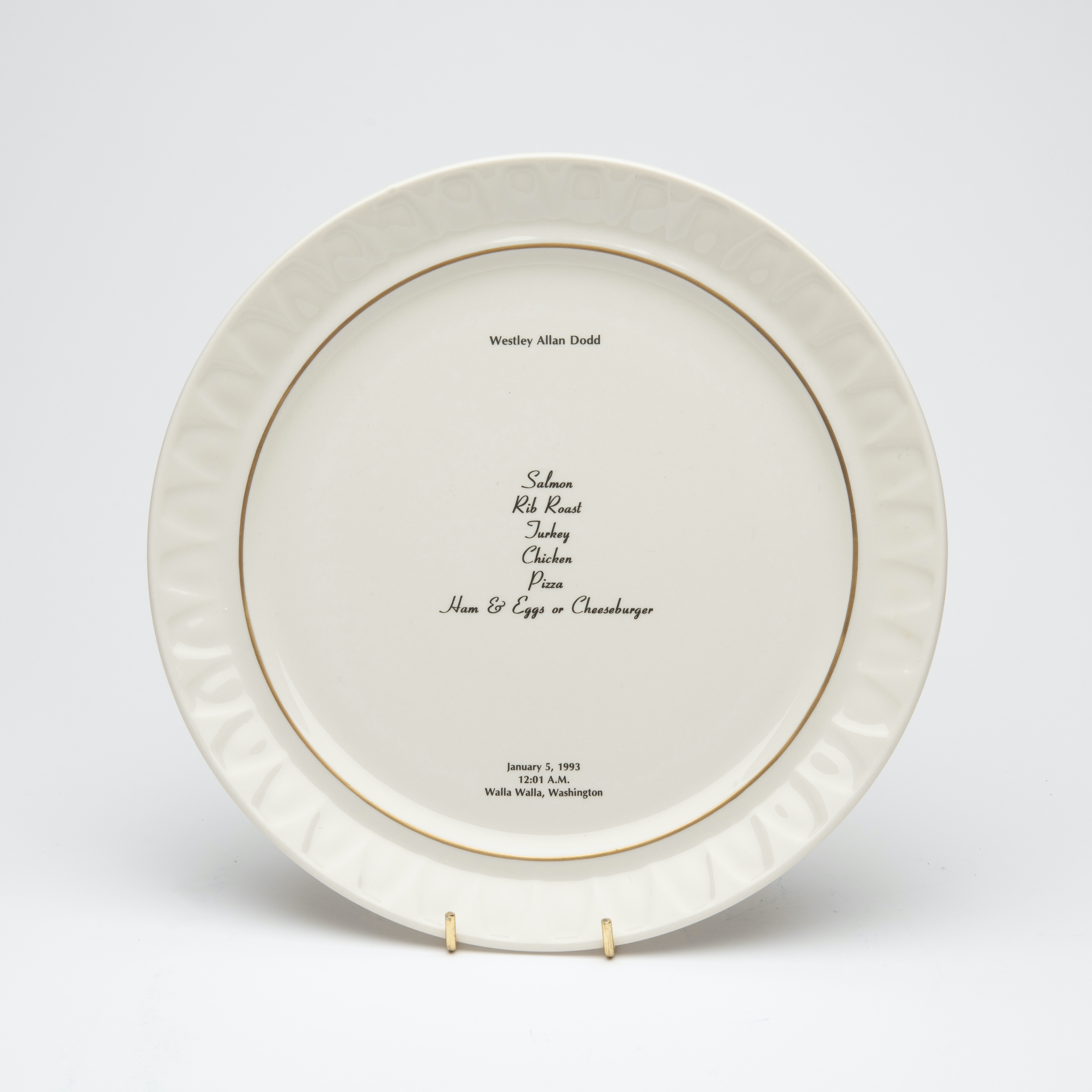 Bone china dinner plate, with gold trim and text printed in center. Text includes a description of the last meal requested and served to someone prior to their execution. The name of the person, time, date and place of execution is also printed on the plate.
