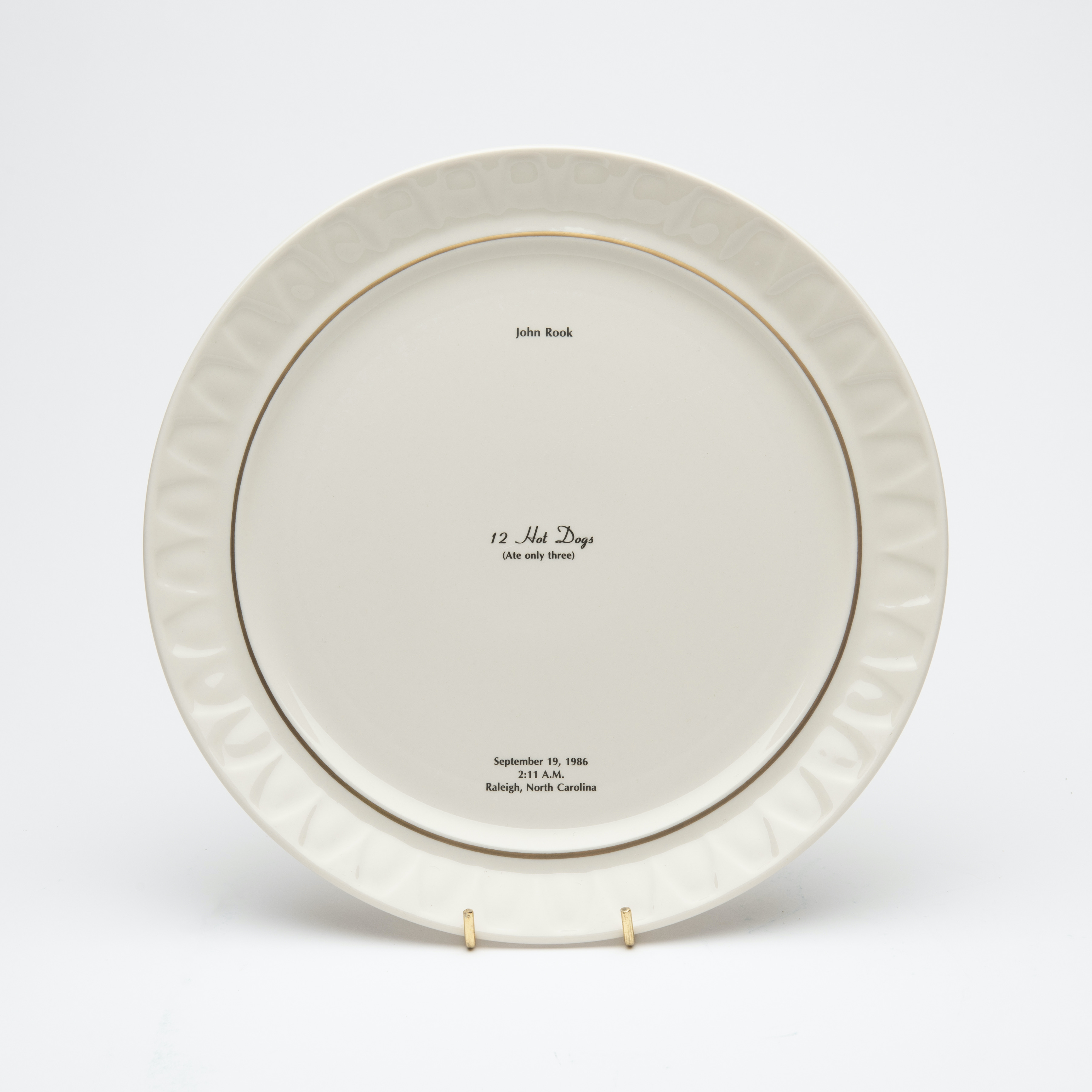 Bone china dinner plate, with gold trim and text printed in center. Text includes a description of the last meal requested and served to someone prior to their execution. The name of the person, time, date and place of execution is also printed on the plate.