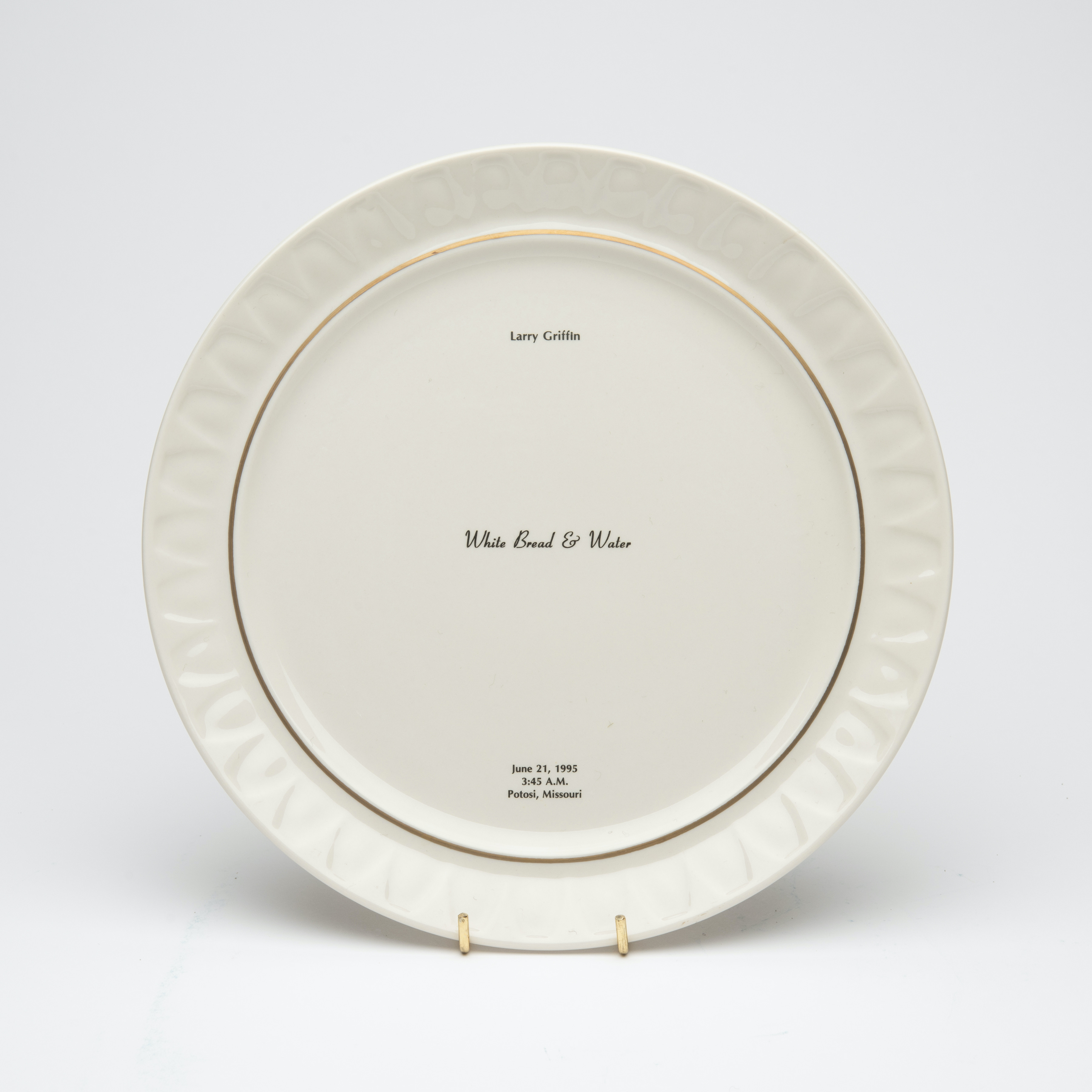 Bone china dinner plate, with gold trim and text printed in center. Text includes a description of the last meal requested and served to someone prior to their execution. The name of the person, time, date and place of execution is also printed on the plate.