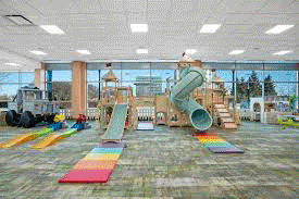The interior of Playroom Cafe Two including pastel slides and wooden climbing equipment, a train table and the café counter in a rotating display of images