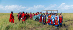A group of Maasai greet a safari tourist in the masai mara, kenya, a retro land rover is behind them